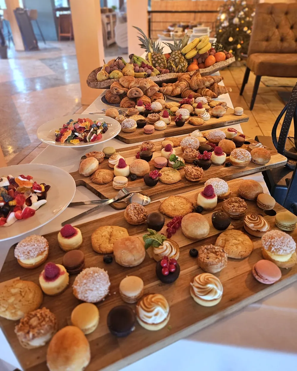 Buffet de réception dressé en salle : pièces sucrées, viennoiseries et fruits sur de longues planches.